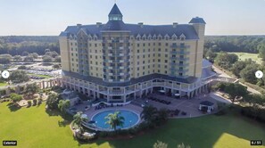 A large hotel with multiple floors, a central courtyard with a swimming pool, and a golf course in the background.