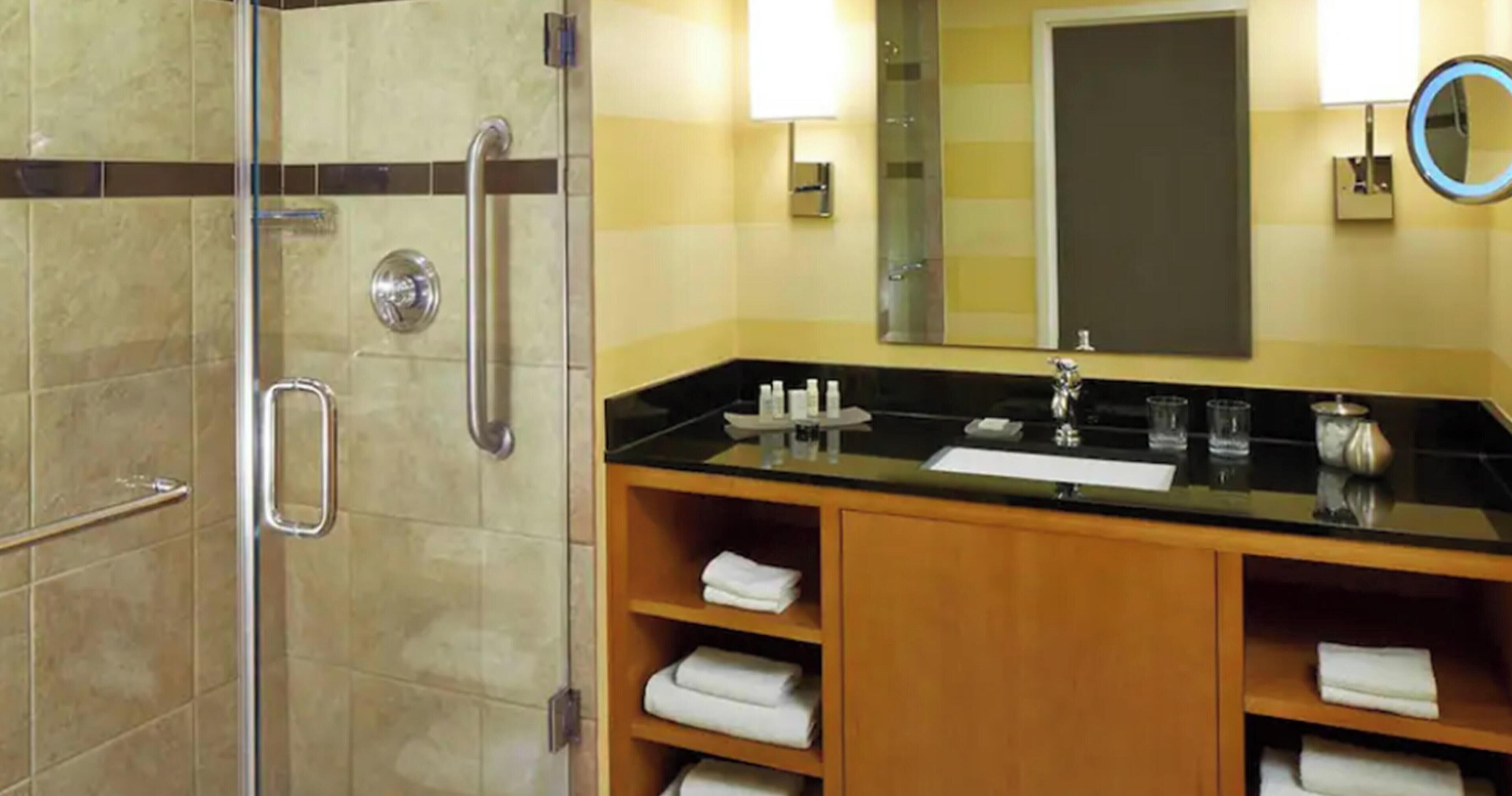 A bathroom with a glass-enclosed shower, a sink with a vanity, and a mirror.