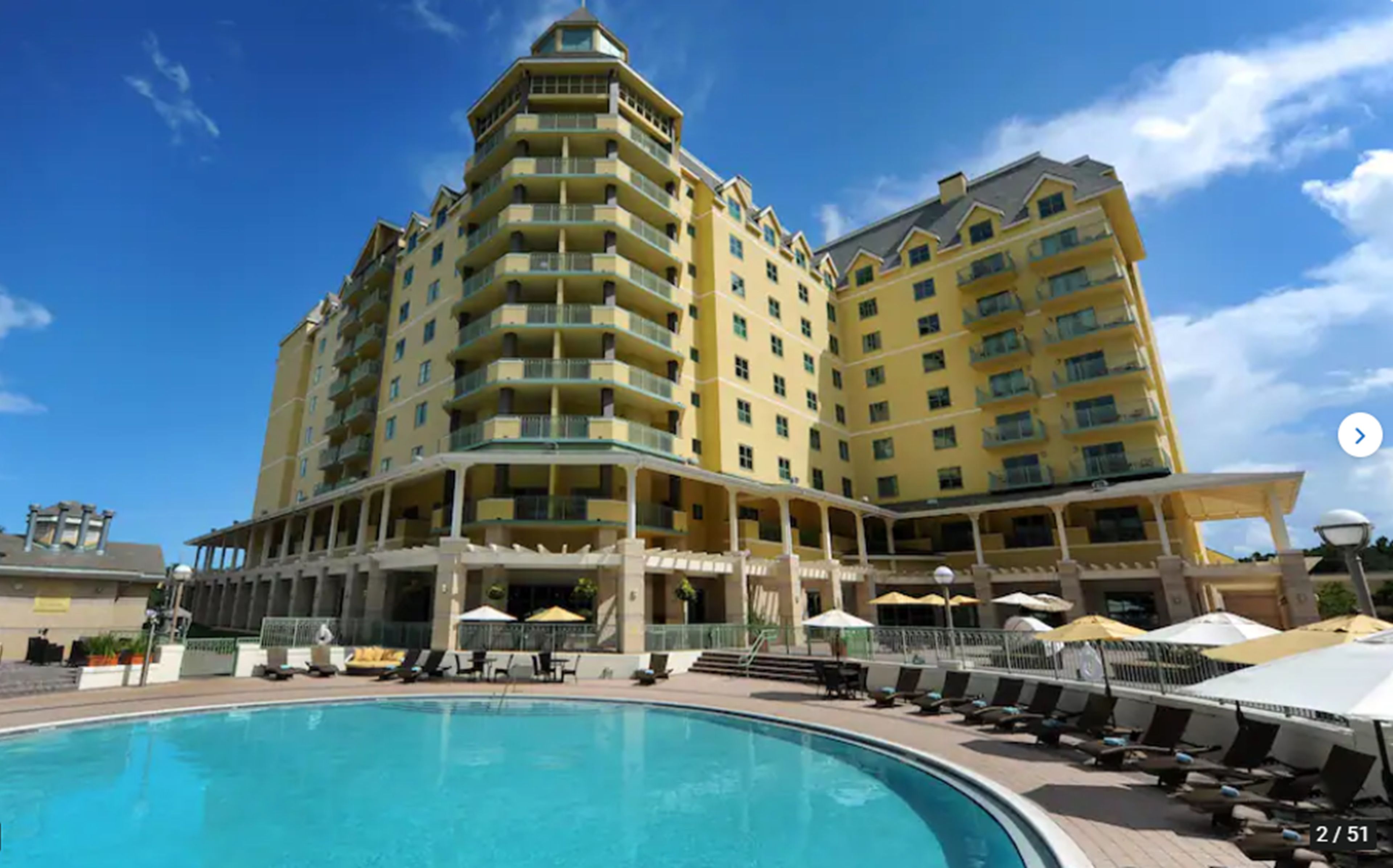 Um hotel com uma piscina grande ao ar livre, várias varandas e um céu azul límpido.