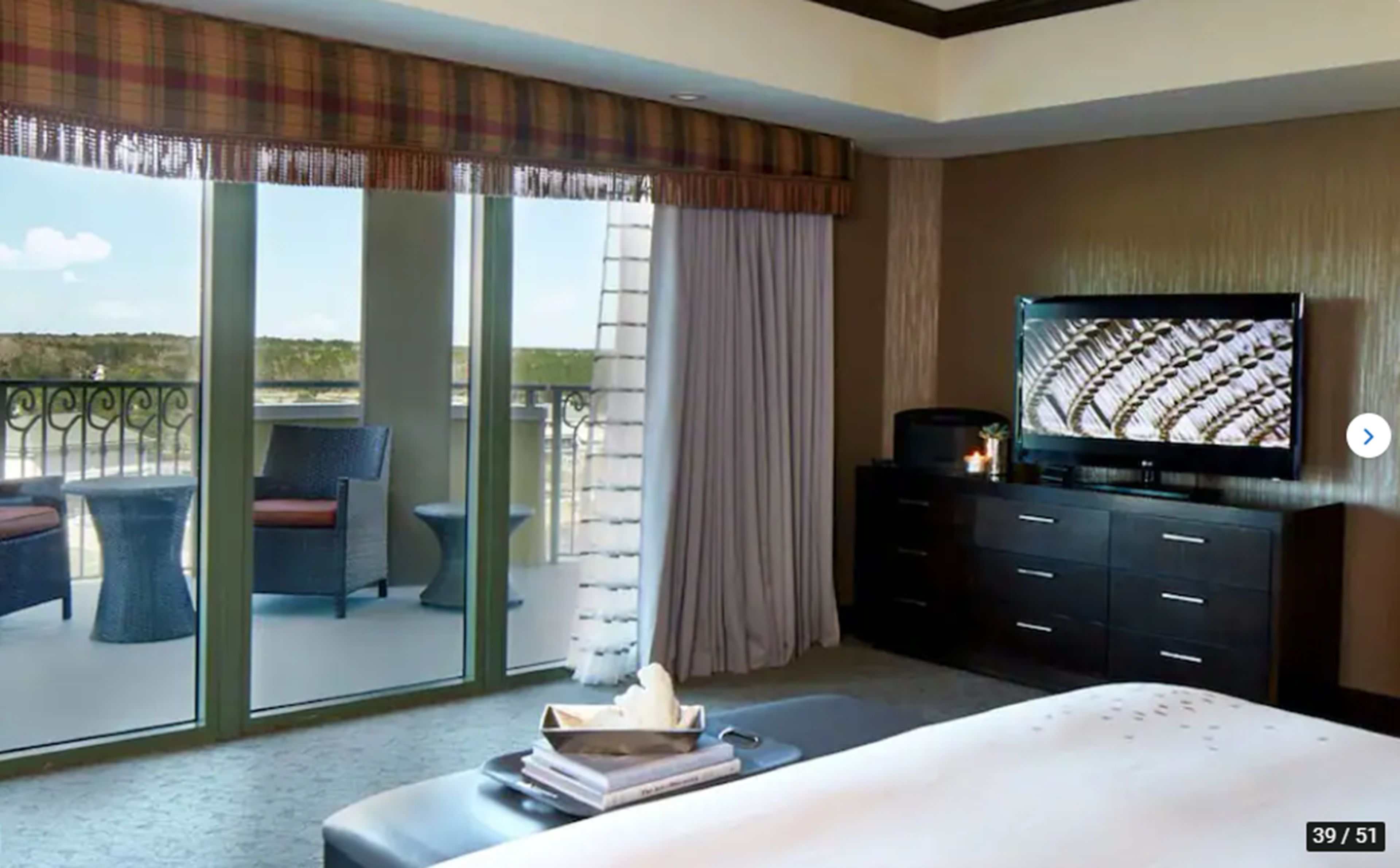 Une chambre d’hôtel avec un balcon, une télévision, un lit et un bureau avec une chaise.