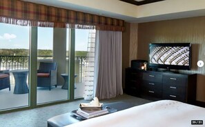 A hotel room with a balcony, a television, a bed, and a desk with a chair.