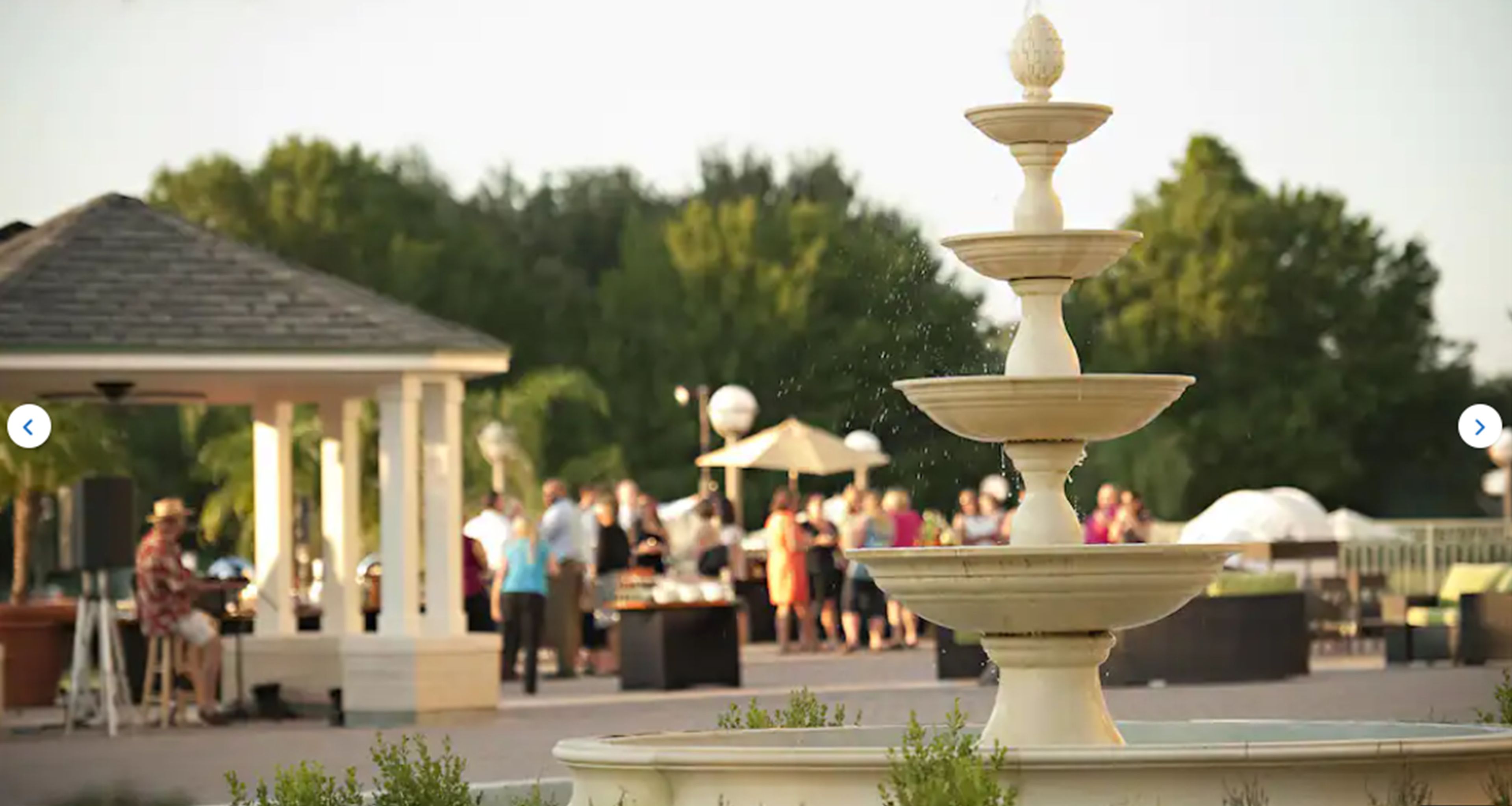 Une fontaine à plusieurs niveaux dans un espace extérieur aménagé pour les banquets, avec un kiosque et des personnes en arrière-plan.