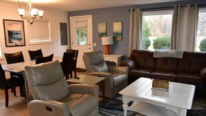 A living room with a brown leather sofa, beige leather chairs, a white coffee table, and a dining area with a wooden table and chairs.