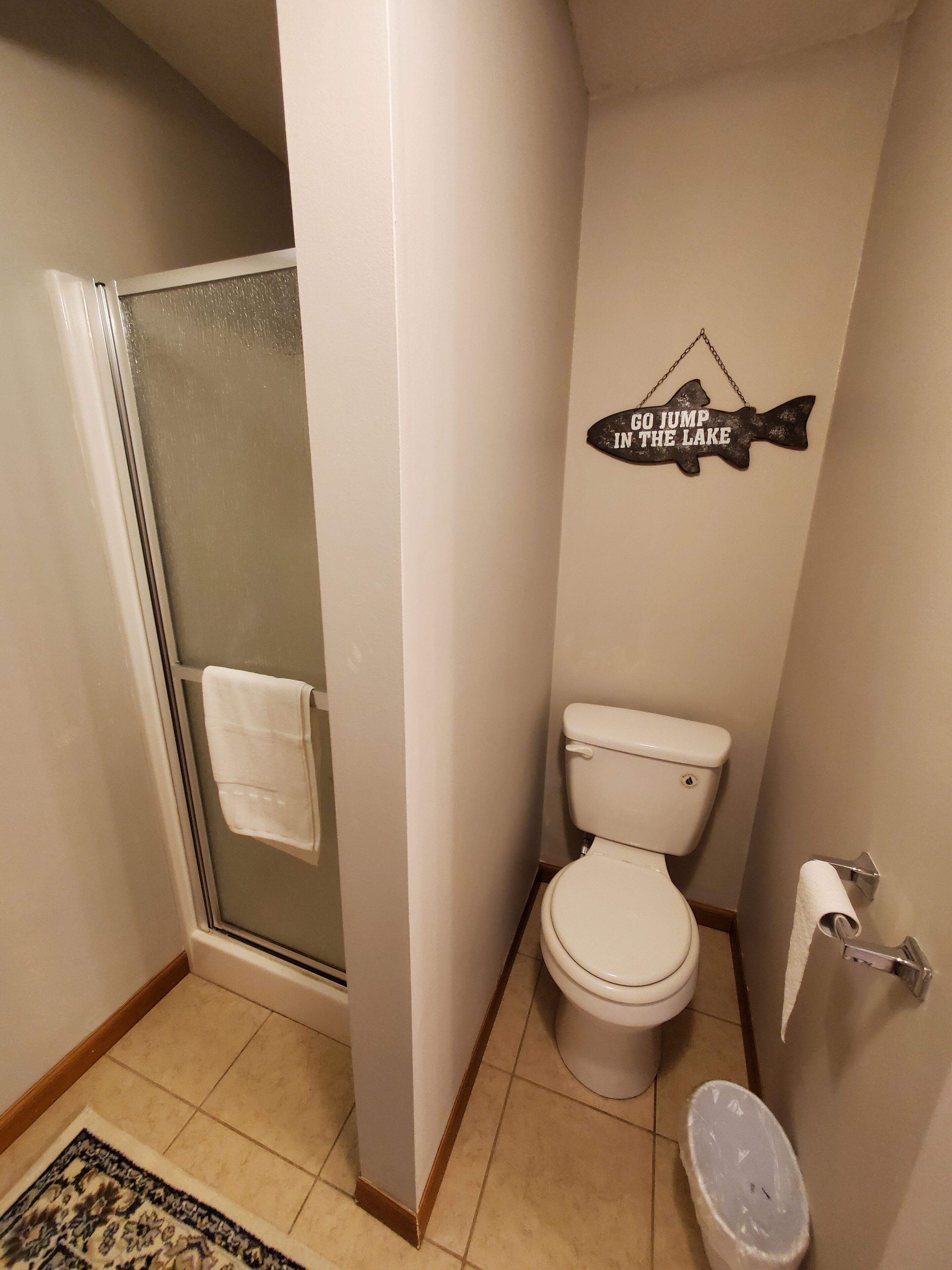 A bathroom with a glass shower enclosure, a toilet, and a wall decal that says "GO JUMP IN THE LAKE".
