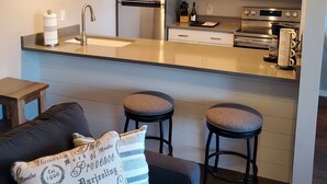 Cocina moderna con electrodomésticos de acero inoxidable, una escalera de madera y una zona de estar acogedora con cojines.