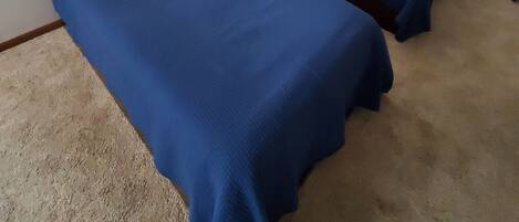 Una habitación con dos camas, cada una con cubrecama azul y almohadas blancas, una mesita de noche con una lámpara, y una pared decorada con objetos que parecen remos.