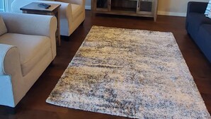 Una sala de estar con una televisión de pantalla plana sobre un soporte de madera, dos sofás color beige, una mesa de centro, una lámpara de pie y una alfombra estampada.