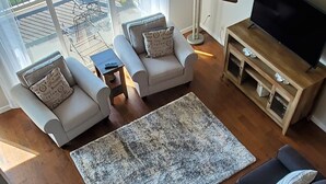 Una sala de estar moderna con una escalera de madera, un ventilador de techo, un televisor y vistas al exterior.