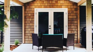 A covered patio with a brick wall, a sliding glass door, and two wicker chairs.