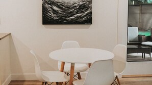 A dining area with a round table and four white chairs with wooden legs, a black and white abstract painting on the wall, and a view of outdoor furniture through a glass door.