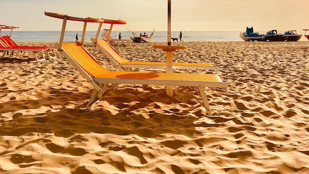 Ein Strand mit Liegestühlen und einem Sonnenschirm.