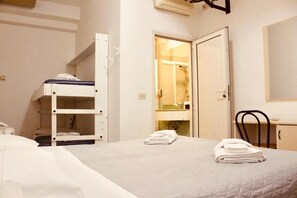Een eenpersoonsbed met een sprei, een stapelbed, een bureau met een stoel, en een badkamer met een spiegel.