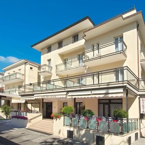 Een hotel met meerdere verdiepingen, met balkons, een overdekte ingang en terrasplekken.