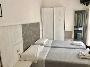 Een hotelkamer met twee bedden, een kledingkast, een badkamer met een wastafel en spiegel, en een raam.