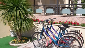 Ein Fahrrad steht neben einem Gebäude mit einem verschlossenen Eingang und einem kleinen Garten mit roten Blumen.