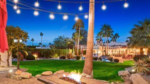 A well-lit outdoor area with a fire feature, palm trees, and a pool.