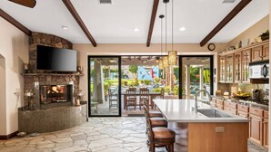 A modern kitchen with a stone fireplace, a large island with bar stools, and a view of the outdoor patio.