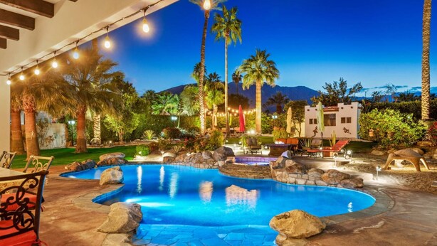 A pool area with a hot tub, lounge chairs, and a stone patio.
