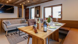 A cozy dining area with a wooden table set for two, a sofa, and a television mounted on the wall. - Atmospheric ski-in/ski-out with terrace (Rauris)