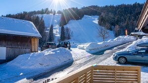 A snowy mountain scene with a clear sky, a wooden building, and parked cars. - Atmospheric ski-in/ski-out with terrace (Rauris)