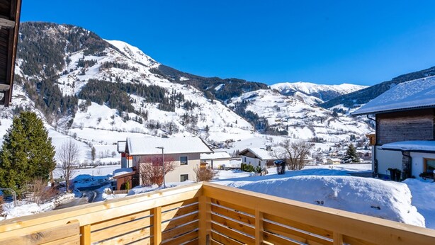 A wooden deck overlooking a snowy mountain landscape with buildings in the foreground. - Atmospheric ski-in/ski-out with terrace (Rauris)