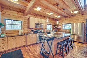 A spacious kitchen with wooden cabinets, a stainless steel refrigerator, and a large island with bar stools. - Modern Log Cabin w/ Rec Room, Steps to Lake! (Pine City)