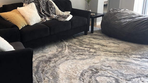 Ein Wohnzimmer mit einer schwarzen Couch, einem gemusterten Teppich, einem kleinen Tisch und einem großen Sitzsack.