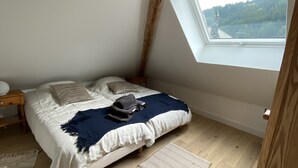 A bedroom with a skylight, wooden flooring, a bed with a blue blanket, and a view of a forested area. - Superb Duplex 8/10 pers 5ch 3sdb 1 balcony 150M2 cocooning in the heart of Queyras (Aiguilles)