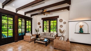 A spacious living room with a high ceiling, large windows, and a ceiling fan.