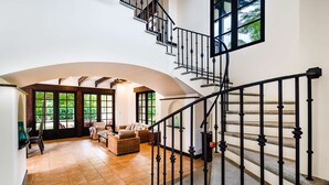 A spacious living area with a curved staircase, large windows, and a view of greenery outside.