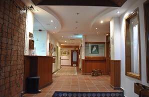 A hotel lobby with a reception desk, a trash bin, a wooden bench, and a tiled floor. - Cerler Edelweiss Apartments (Benasque)