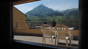 Un balcó amb dues cadires de plàstic blanc i una taula, amb vista a un paisatge de muntanyes.
