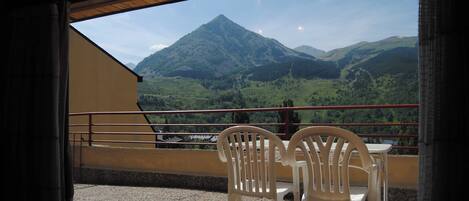 A balcony with two white plastic chairs and a table, overlooking a mountainous landscape.