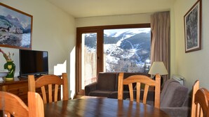 Una zona de menjador amb una taula i cadires de fusta, una televisió i vista a un paisatge nevà a través d'una finestra gran.