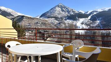 Un balcón con una mesa y sillas blancas, con vista a un paisaje montañoso nevado.