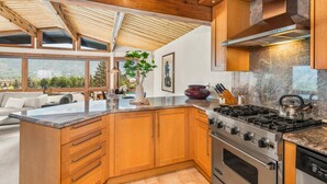 Een moderne keuken met houten kastjes, een groot eiland, een gasfornuis en uitzicht op de omgeving.