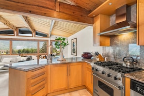 A modern kitchen with wooden cabinets, a large island, a gas stove, and a view of the outdoors.