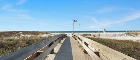 A wooden boardwalk leading to a beach with a sandy shore and a clear blue sky.