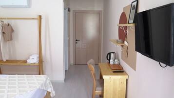 Un dormitorio con una cama, un escritorio de madera, una silla, un televisor y una puerta que da a otra habitación.