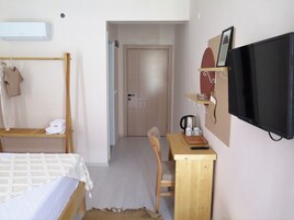 Un dormitorio con una cama, un escritorio de madera, una silla, un televisor y una puerta que da a otra habitación.