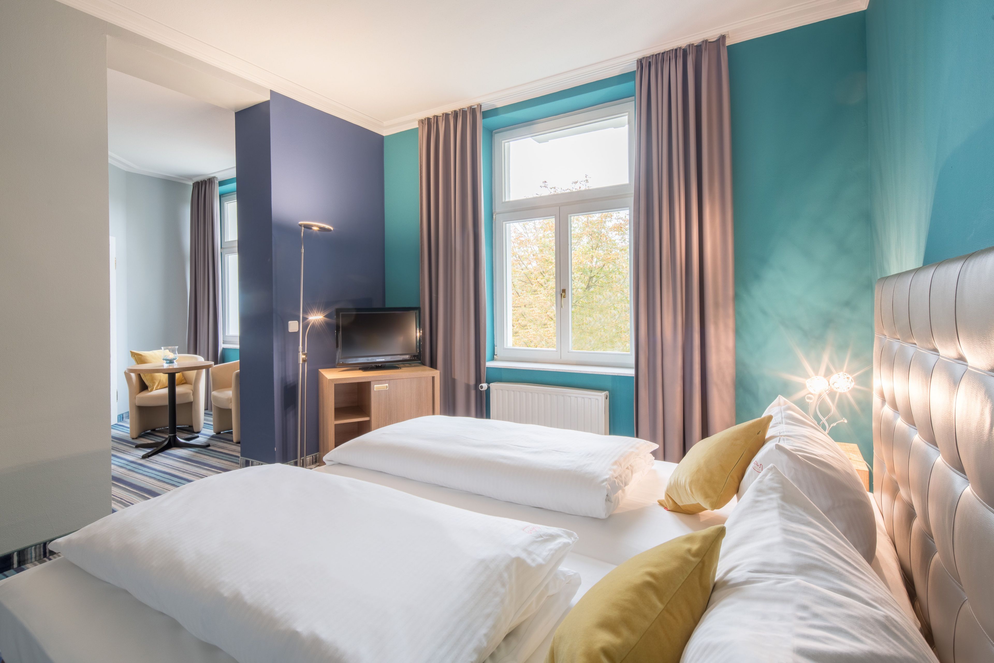 Ein Hotelzimmer mit Bett, Schreibtisch, Stuhl und einem Fenster mit Vorhängen.
