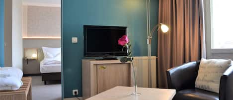 A hotel room with a bed, a television, a table with a vase, a lamp, and a sofa.