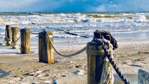 Un poste de madera con una cuerda, situado en una playa arenosa con olas al fondo.