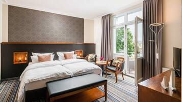 Ein Hotelzimmer mit einem großen Bett, einem Schreibtisch, einem Sessel, einer Bank, einem Fernseher und einem Balkon mit Vorhängen.
