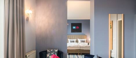 Une chambre d’hôtel avec un lit, une table ronde ornée d’un vase de fleurs, une chaise, un miroir et une lampe fixée au mur.