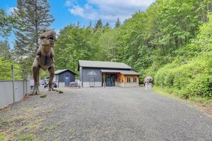 Un bâtiment avec une allée gravillonnée, un espace clôturé et une grande statue de dinosaure.