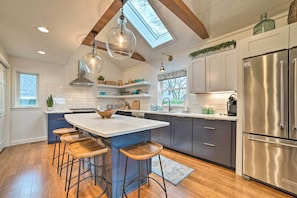 A modern kitchen with a central island, bar stools, a stainless steel refrigerator, and a skylight. - Chic Manistee Cottage: Steps to Lake Michigan! (Manistee)