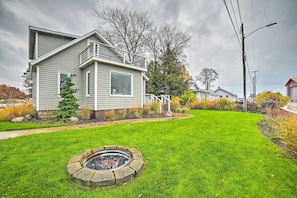 A two-story house with a fire pit in the front yard, surrounded by a well-maintained lawn and various plants. - Chic Manistee Cottage: Steps to Lake Michigan! (Manistee)