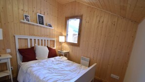 Ein Schlafzimmer mit einer holzverkleideten Wand, einem weißen Bett mit roten und weißen Kissen, einem Nachttisch mit einer Lampe und einem Fenster.