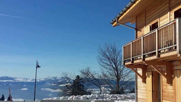 Eine Holzhütte mit Balkon mit Blick auf eine verschneite Landschaft und Berge.